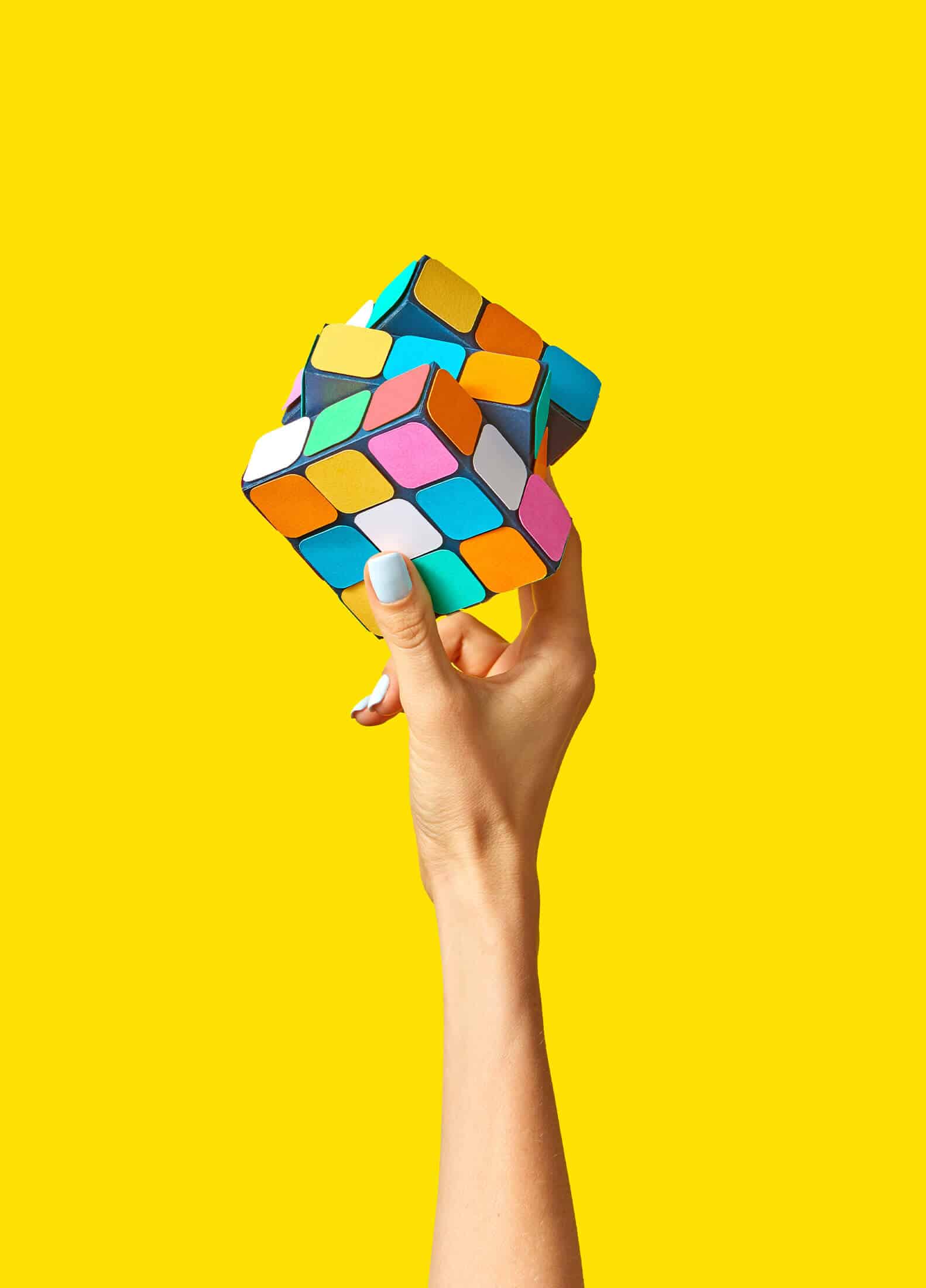 Isolated hand holding a rubik's cube in front of a bright yellow background